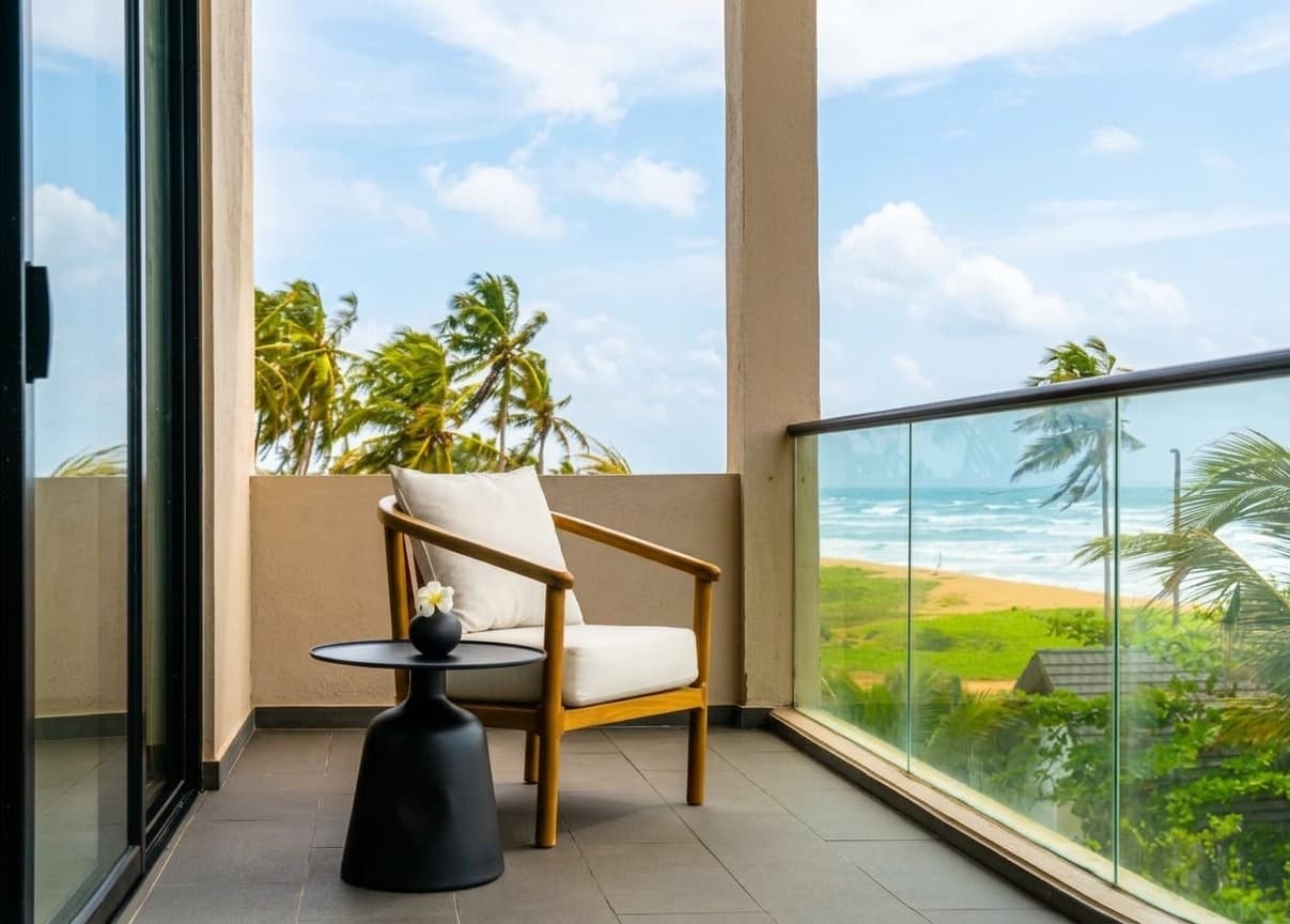 Photograph of the balcony of a sea-view Deluxe Room, looking past coconut palms to the beach and the Indian Ocean.